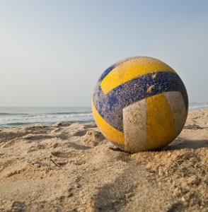 a yellow, white, and blue beach volleyball sits on the sand with the ocean in the background
